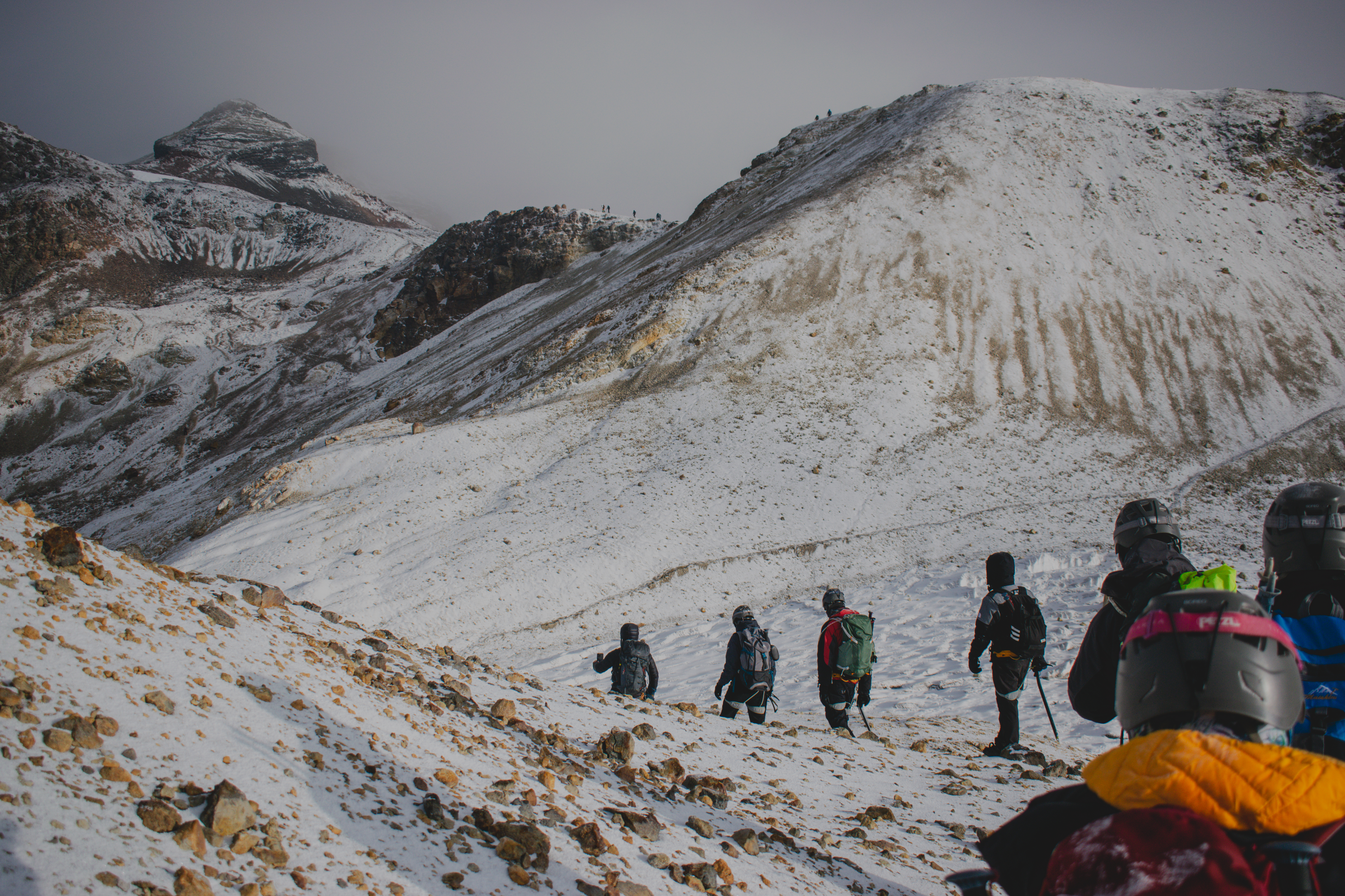 Group of climbers ascending a snowy volcanic slope under dramatic winter light