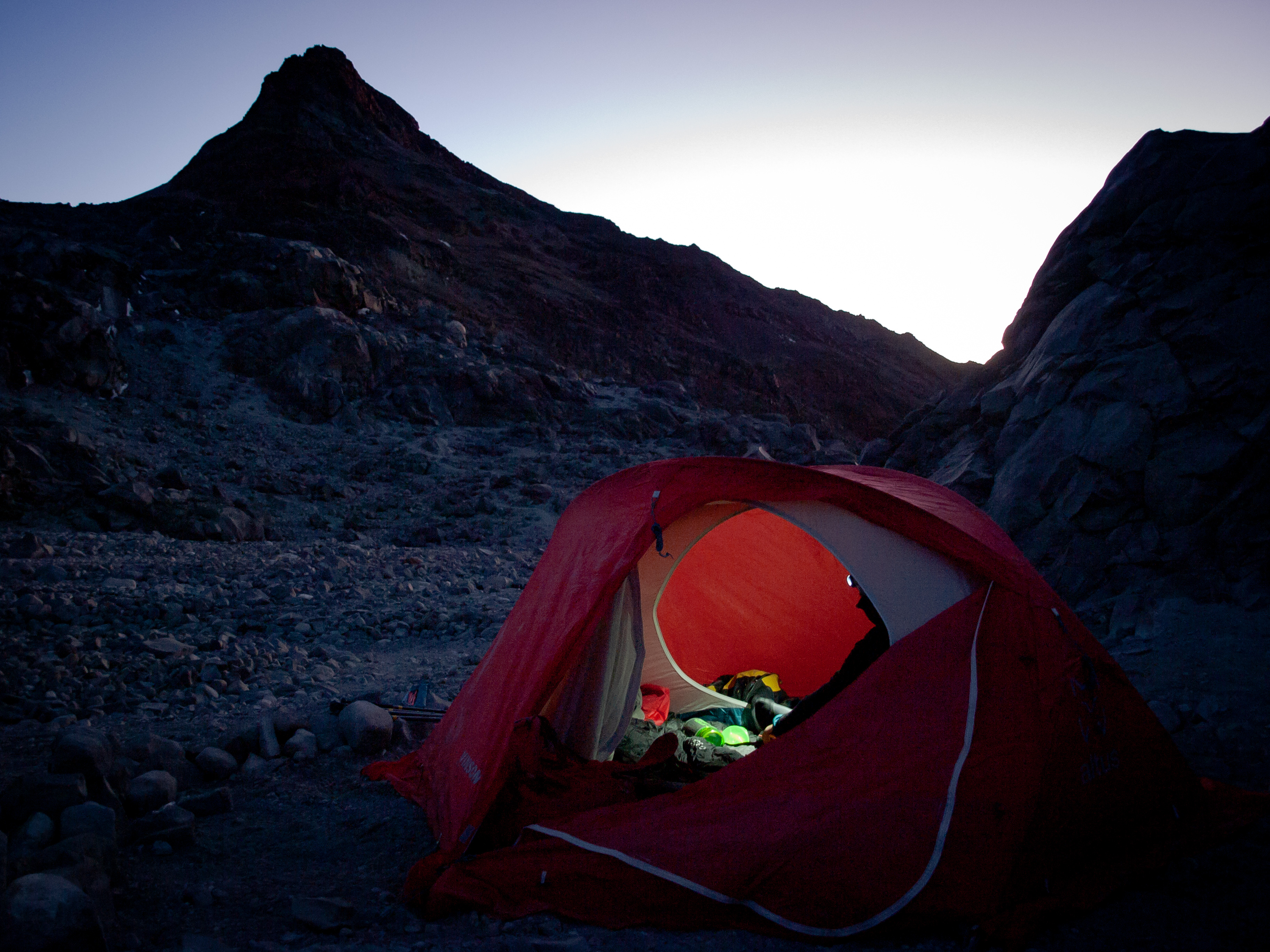 Red tent glowing at high camp under the dark volcanic silhouette at twilight