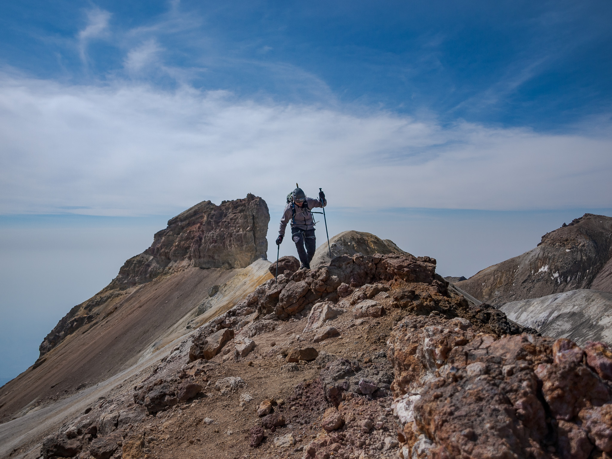 Climber walking the crater rim ridge of Pico de Orizaba — blue sky, clouds below