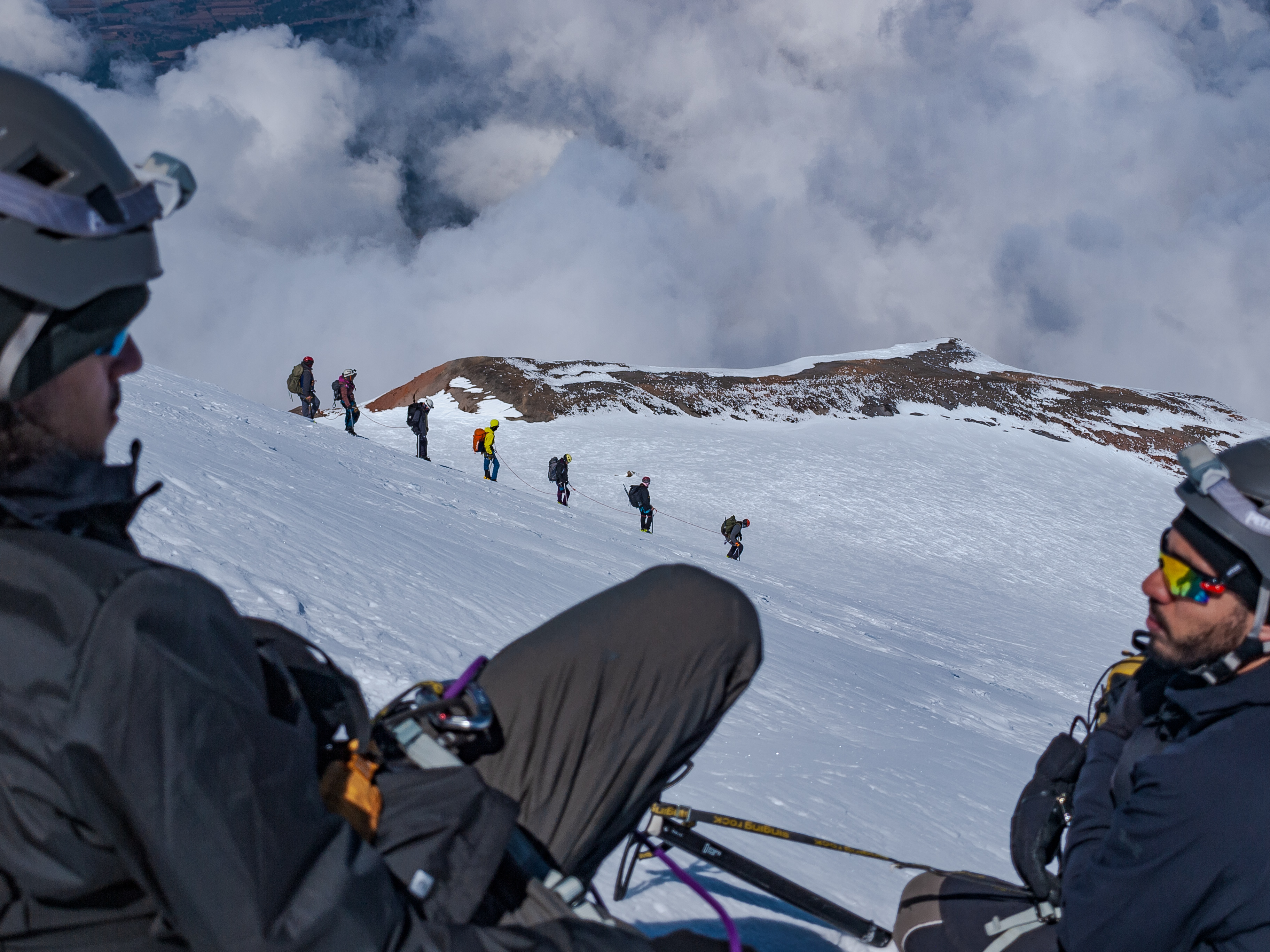Climbers resting on the blue ice, viewed from above — the rope connecting them across the slope