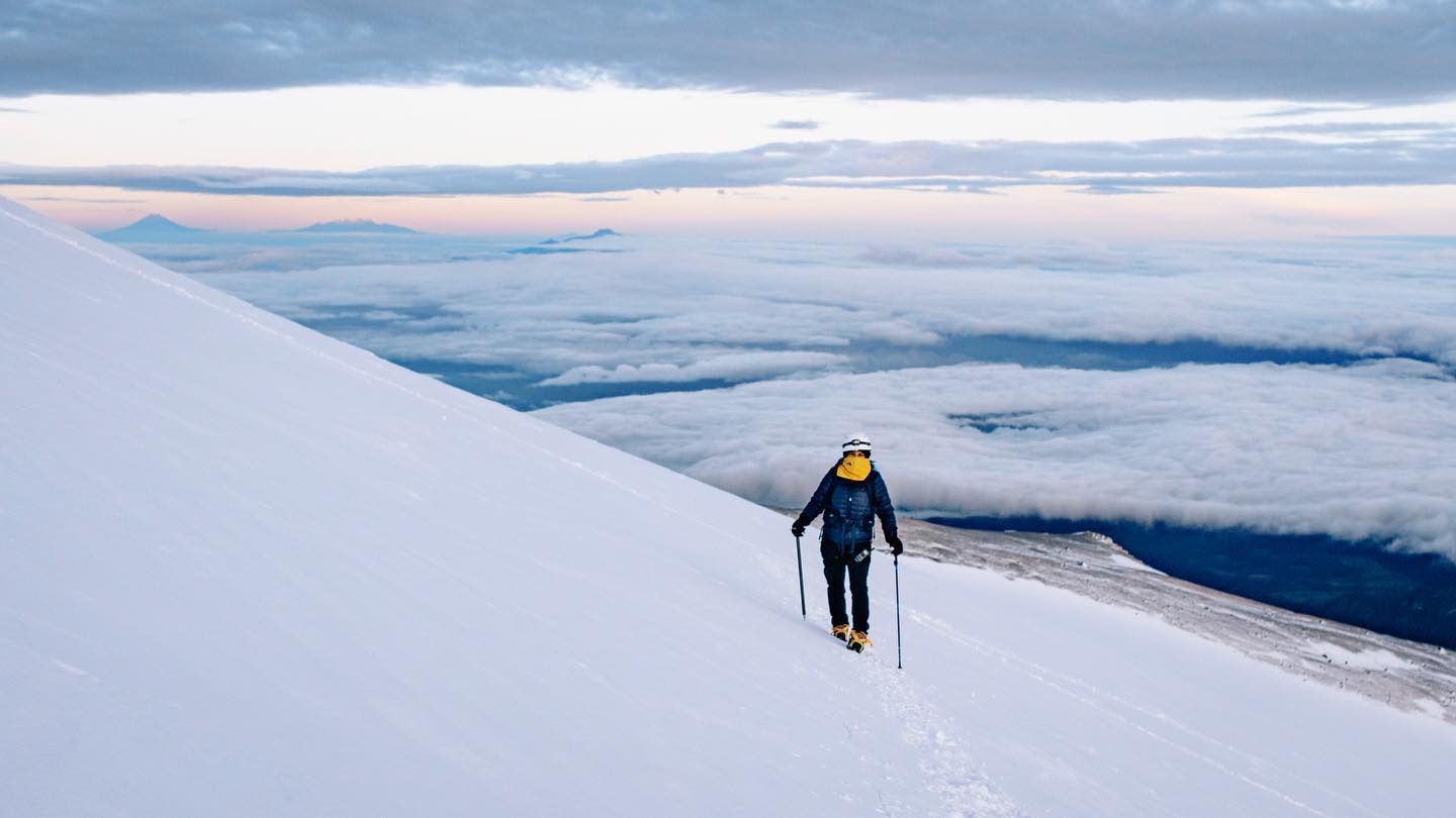Lone climber ascending Pico de Orizaba glacier above a sea of clouds at dawn