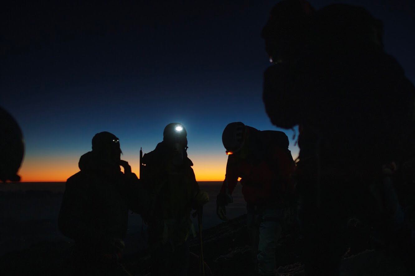 Climbers silhouetted with headlamps before the overnight summit push — the last light on the horizon