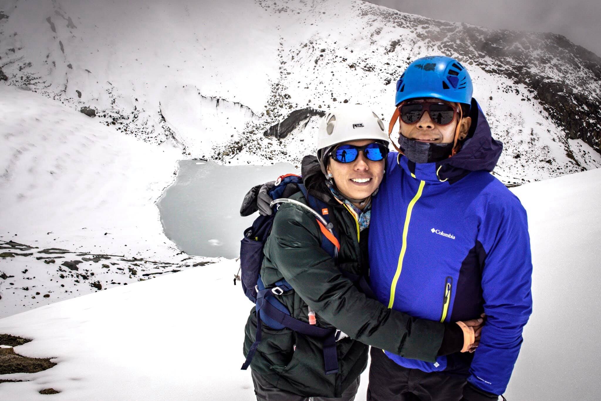 Two climbers celebrating at the summit — smiling, helmeted, gear on